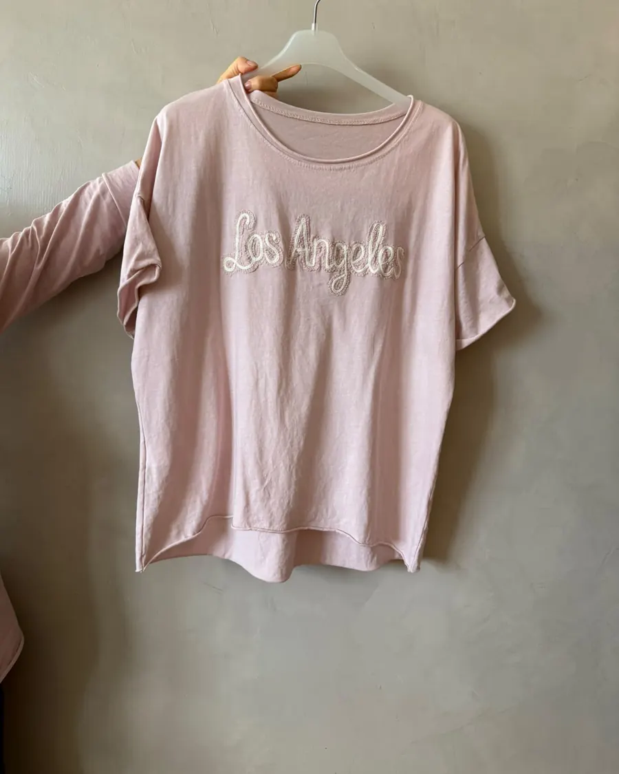 Remera rosa con bordado colgada en una percha